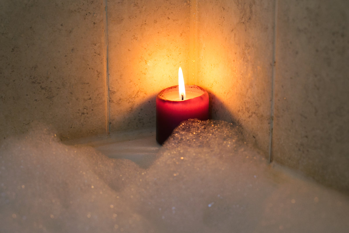 Brennende Kerze am Rand einer Badewanne mit Schaum
